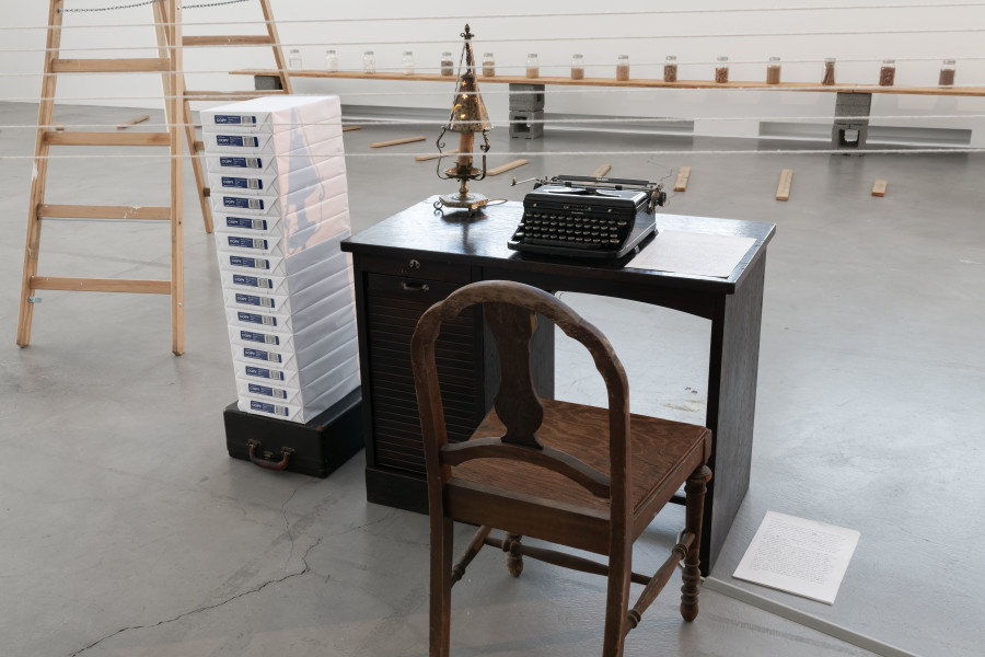 Renée Green, Sites of Genealogy (Fear, Flight, Fate; Matrix; Loophole of Retreat), 1990, Installation across three locations in the museum. Mixed Media: wooden table, chair, typewriter, lamp, stack of blank paper, paper with typed text, wooden ladder, telescope, cotton string, muslin drape, silkscreen, rubber-stamped wooden slats, vinyl type and puzzle pieces on vellum, jars with varied colored contents on wooden shelf with vinyl type, plaques with rubber-stamped text with puzzle pieces, jars and wheelbarrow filled with coal, rubber-stamped sourcebook, rubber-stamped wooden shelf, rotating red light, sound. Collection of the artist; Courtesy Free Agent Media; Bortolami Gallery, New York; Galerie Nagel Draxler, Berlin/Cologne/Munich. Photo: Flavio Karrer.