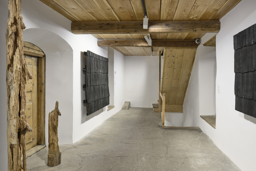 Exhibition view, Augustas Serapinas, Roof of a House from Steponių Village, 2022, charred reclaimed wooden shingle roof Part of the House from Skirgiškės, 202, reclaimed wood. Photo: Ralph Feiner, Courtesy of the artist and Galerie Tschudi