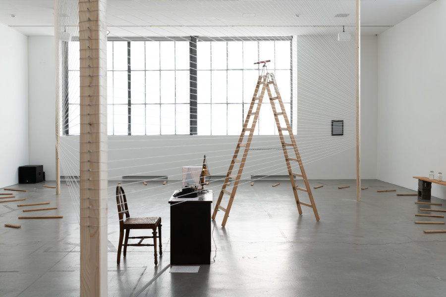 Renée Green, Sites of Genealogy (Fear, Flight, Fate; Matrix; Loophole of Retreat), 1990, Installation across three locations in the museum. Mixed Media: wooden table, chair, typewriter, lamp, stack of blank paper, paper with typed text, wooden ladder, telescope, cotton string, muslin drape, silkscreen, rubber-stamped wooden slats, vinyl type and puzzle pieces on vellum, jars with varied colored contents on wooden shelf with vinyl type, plaques with rubber-stamped text with puzzle pieces, jars and wheelbarrow filled with coal, rubber-stamped sourcebook, rubber-stamped wooden shelf, rotating red light, sound. Collection of the artist; Courtesy Free Agent Media; Bortolami Gallery, New York; Galerie Nagel Draxler, Berlin/Cologne/Munich. Photo: Flavio Karrer.