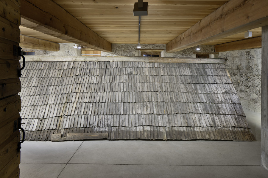 Exhibition view, Augustas Serapinas, Upper Roof Part of the House from Steponių Village, 2022, charred reclaimed wooden shingle roof, 180 x 640 x 340 cm. Photo: Ralph Feiner, Courtesy of the artist and Galerie Tschudi