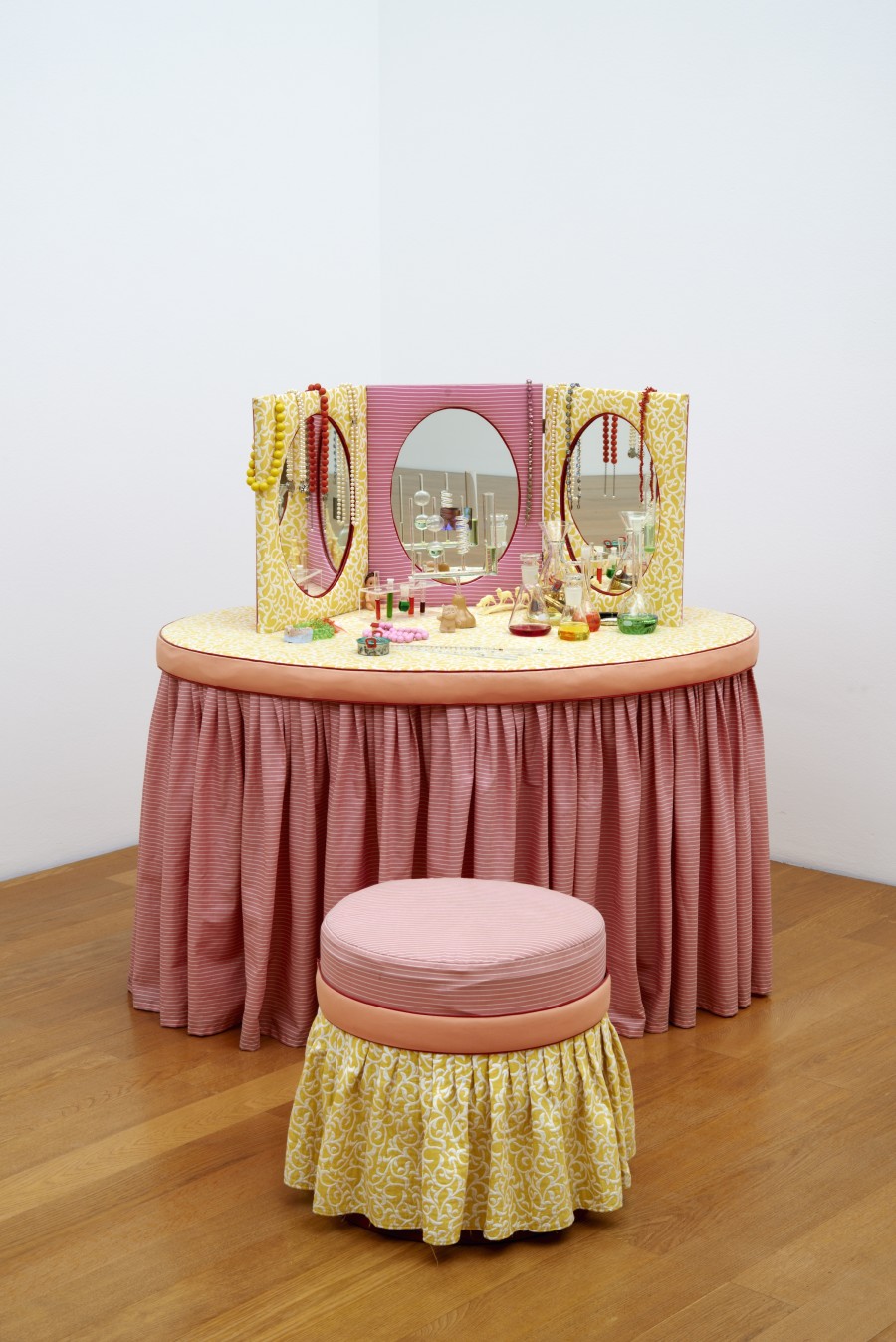 Pipilotti Rist Schminktischlein mit Feedback, 1993 | Makeup table with feedback, 1993 Tisch, mit Stoff verkleidet, Spiegelaufsatz mit integriertem Monitor, 3 Erlenmeyer-Kolben mit Lebensmittelfarblösung (gelb, rot, blau), Glaskondensator, Pipetten, Modeschmuck, Lippenstifte, Kinderspielzeug (Puppe, Plüschtier, Kochtopf, Plastiktier), Gebiss 80 × 120 × 120 cm (Tisch) Kunstmuseum Liechtenstein, Vaduz Erworben mit Mitteln der "Stiftung Freunde des Kunstmuseum Liechtenstein" | purchased with funds from "Stiftung Freunde des Kunstmuseum Liechtenstein" © 2021, ProLitteris, Zürich
